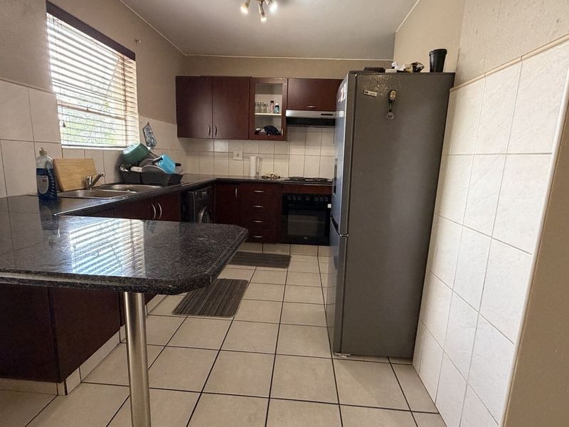 Functional kitchen featuring dark wood cabinetry, granite countertops, tiled backsplash, and built-in cooking appliances with a breakfast bar area.