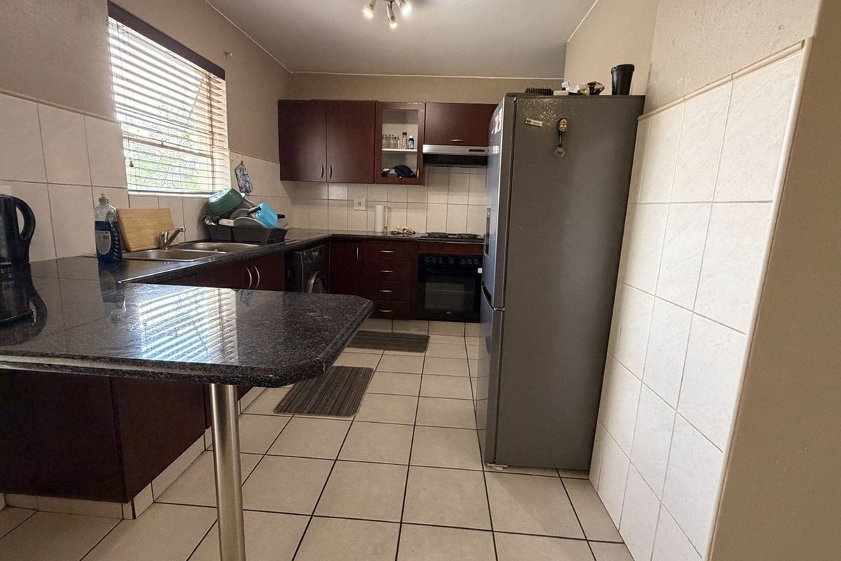 Functional kitchen featuring dark wood cabinetry, granite countertops, tiled backsplash, and built-in cooking appliances with a breakfast bar area.