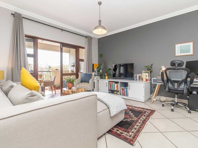 A bright living room featuring tiled flooring, crown molding, and a sliding glass door providing access to an outdoor balcony area.