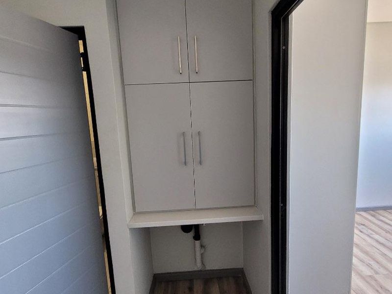 A compact laundry nook featuring built-in cabinetry and dedicated plumbing connections, finished with modern laminate flooring.