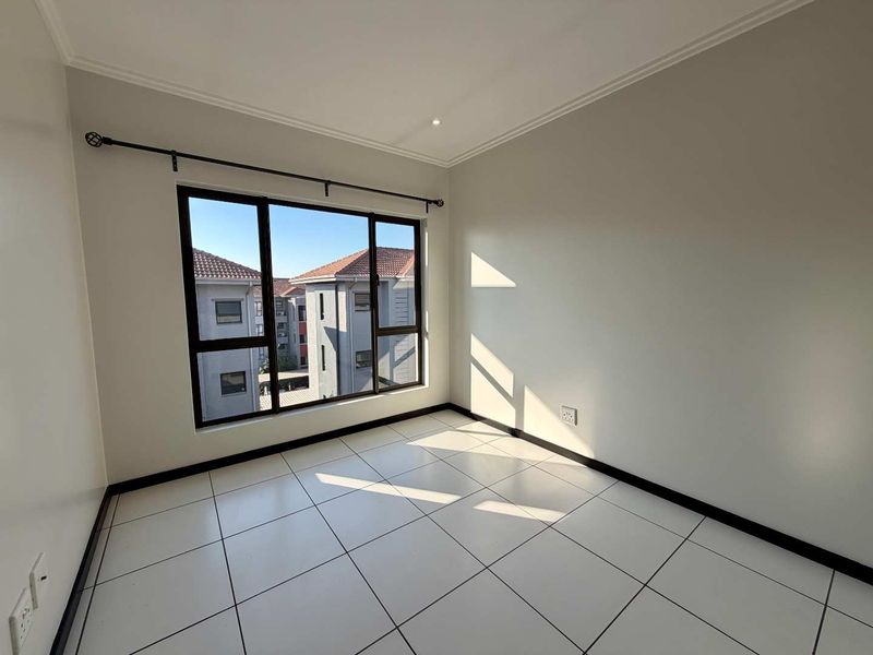 A bright, empty bedroom featuring neutral tiled flooring, clean walls, and large aluminium-framed windows with an installed curtain rod.