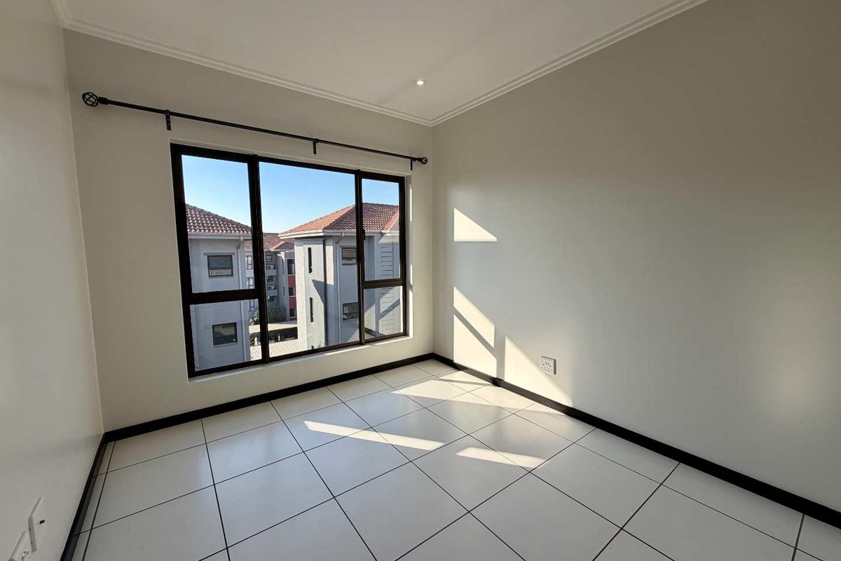 A bright, empty bedroom featuring neutral tiled flooring, clean walls, and large aluminium-framed windows with an installed curtain rod.
