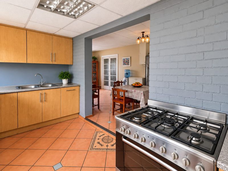 A functional kitchen featuring light wood cabinetry, a stainless steel gas stove, and tiled flooring, with an open-plan layout connecting to the dining area.