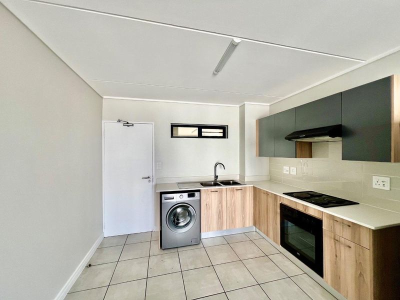Modern kitchen featuring light wood-finish cabinetry, stone-look countertops, integrated appliances, and tiled flooring in a clean, open-plan layout.