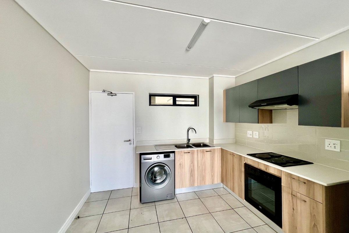 Modern kitchen featuring light wood-finish cabinetry, stone-look countertops, integrated appliances, and tiled flooring in a clean, open-plan layout.