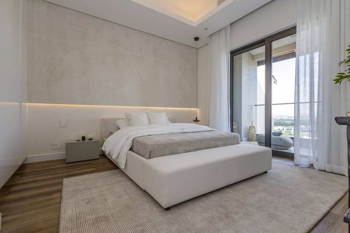 Modern bedroom featuring recessed ceiling lighting, textured feature wall, wood-look flooring, and large sliding glass doors opening to a private balcony.