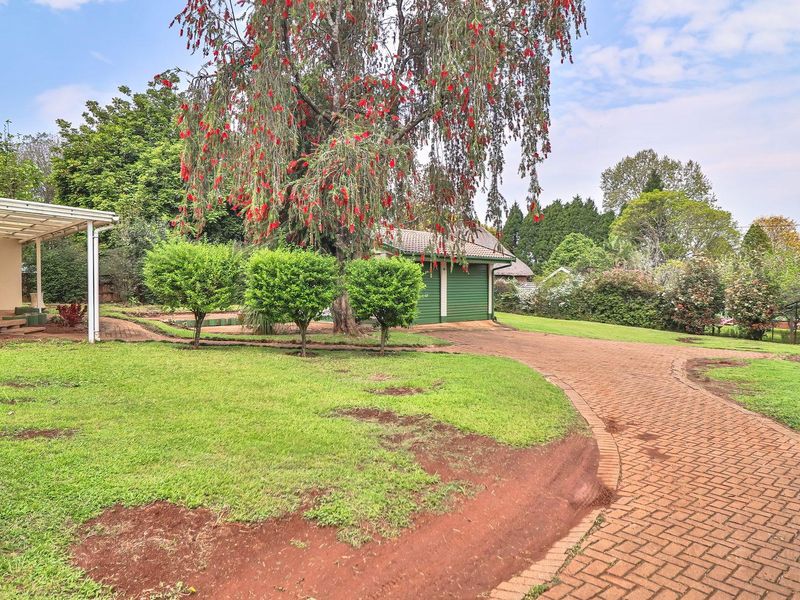 A spacious rear garden featuring a paved driveway, a covered patio area, and a detached garage set within a well-established landscaped yard.
