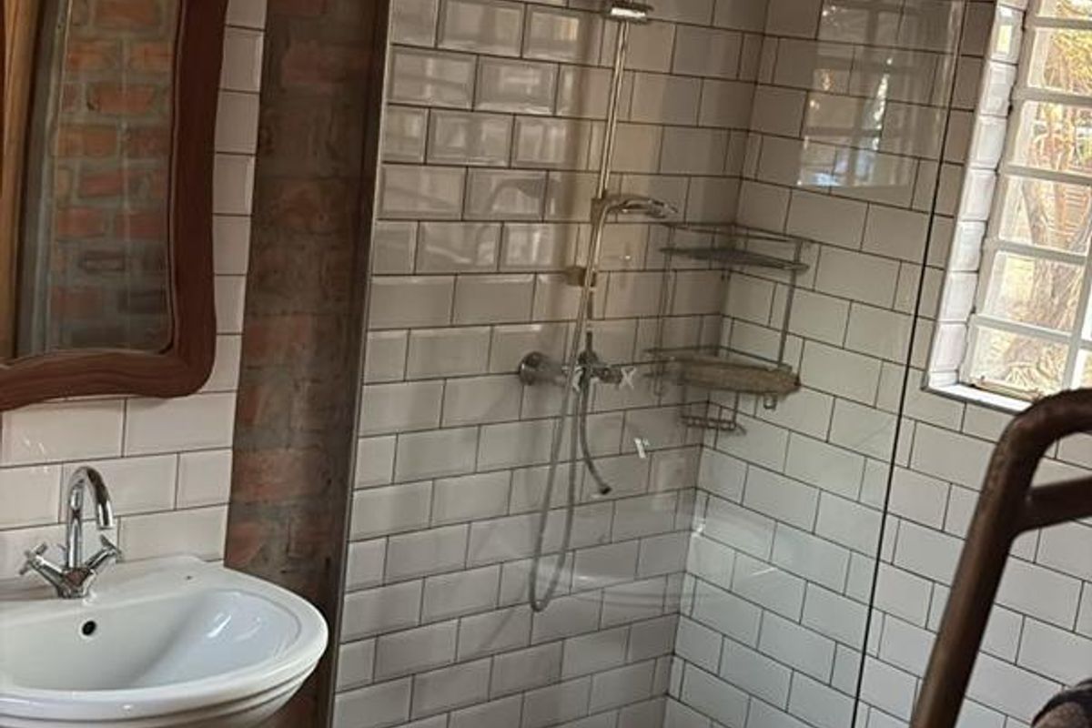 A rustic-style bathroom featuring a walk-in shower with subway tile surround, pebble-stone flooring, and a classic pedestal sink.