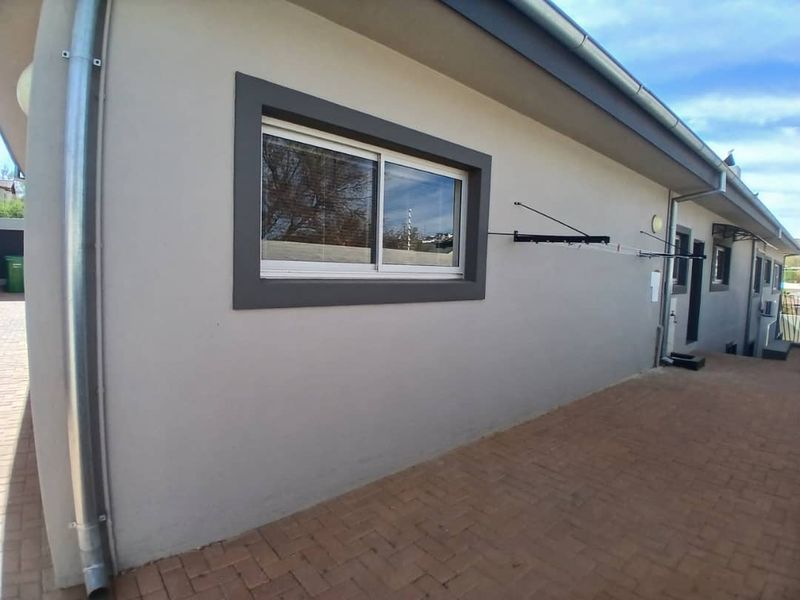 A clean rear exterior view of the property featuring paved patio flooring, a sliding window with dark trim, and a wall-mounted clothesline.