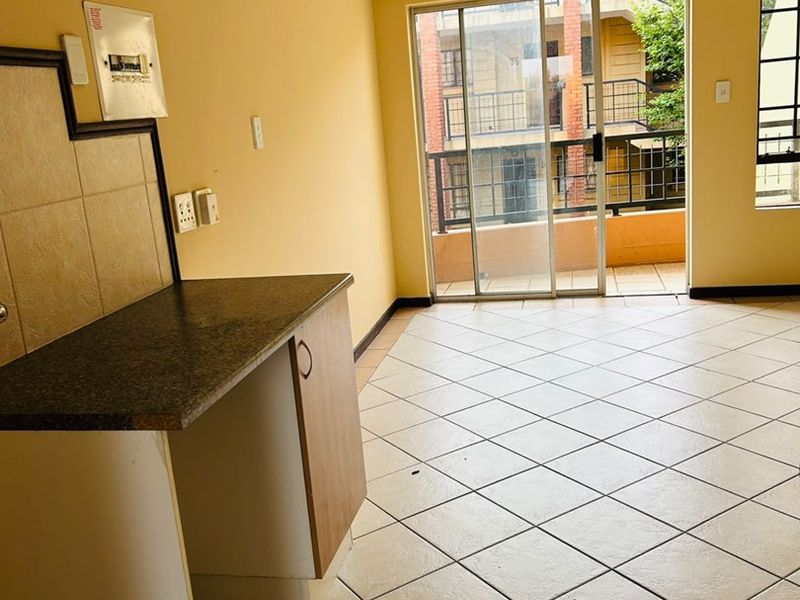 An empty open-plan living area featuring tiled flooring, a small kitchen counter, and a sliding glass door leading to a balcony.