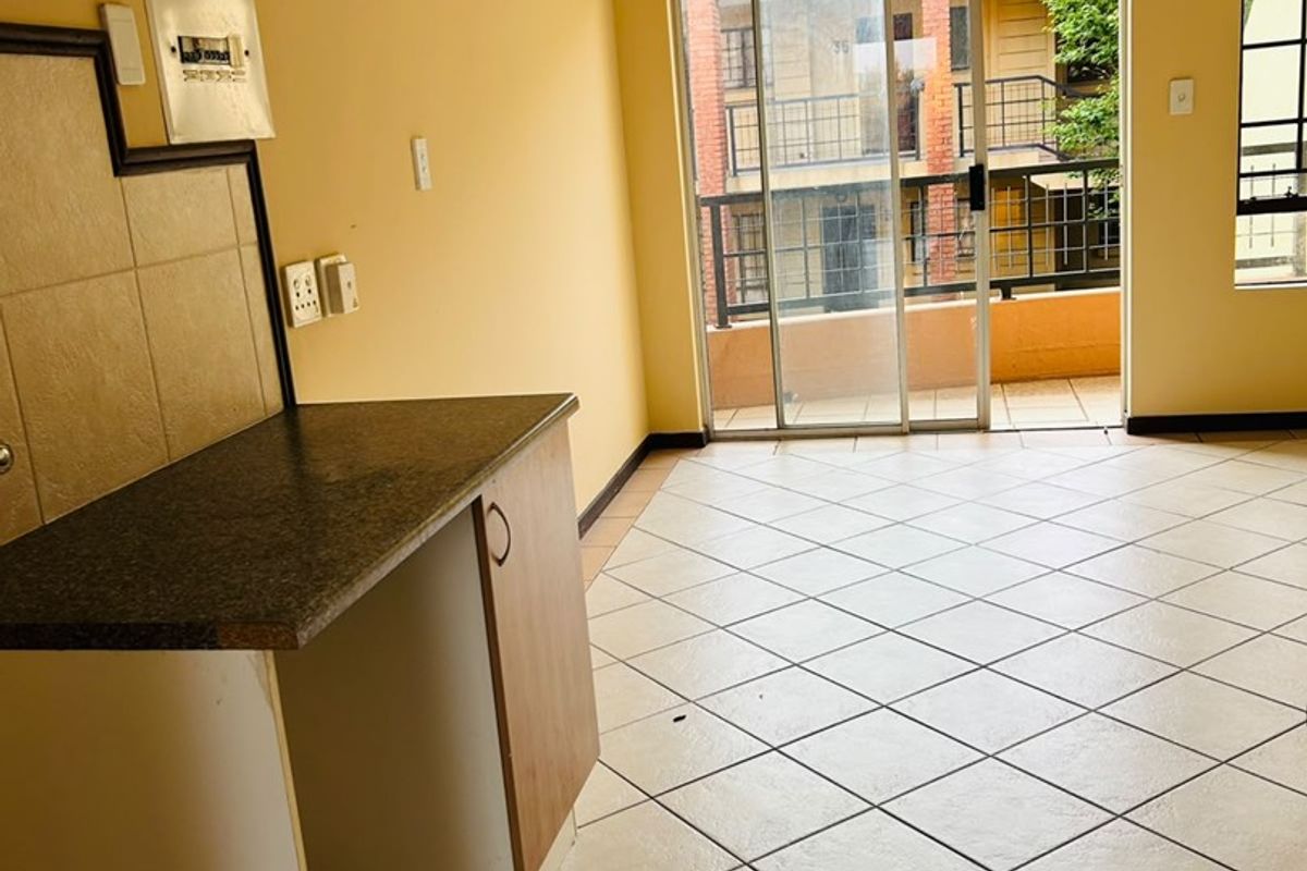 An empty open-plan living area featuring tiled flooring, a small kitchen counter, and a sliding glass door leading to a balcony.