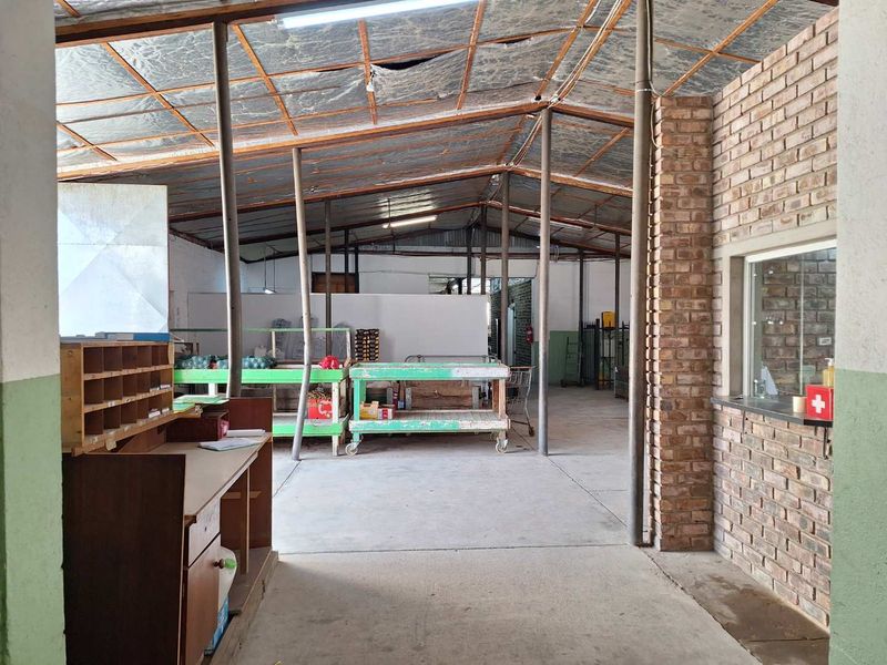 A spacious industrial utility area featuring exposed brickwork, concrete flooring, and a high metal roof structure, suitable for storage or workshop operations.