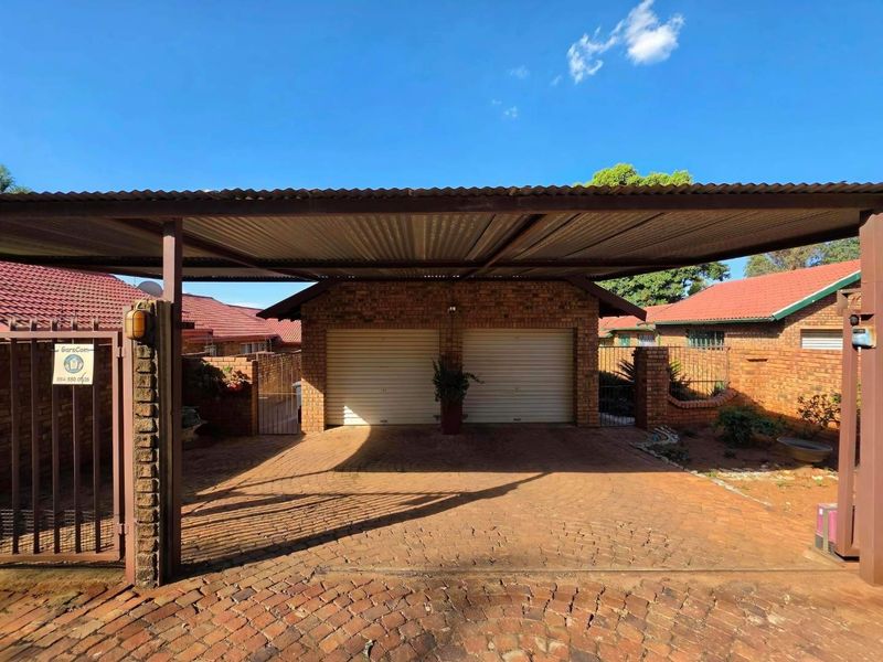A double garage with a corrugated metal carport and brick-paved driveway, featuring facebrick construction and secure gated access.
