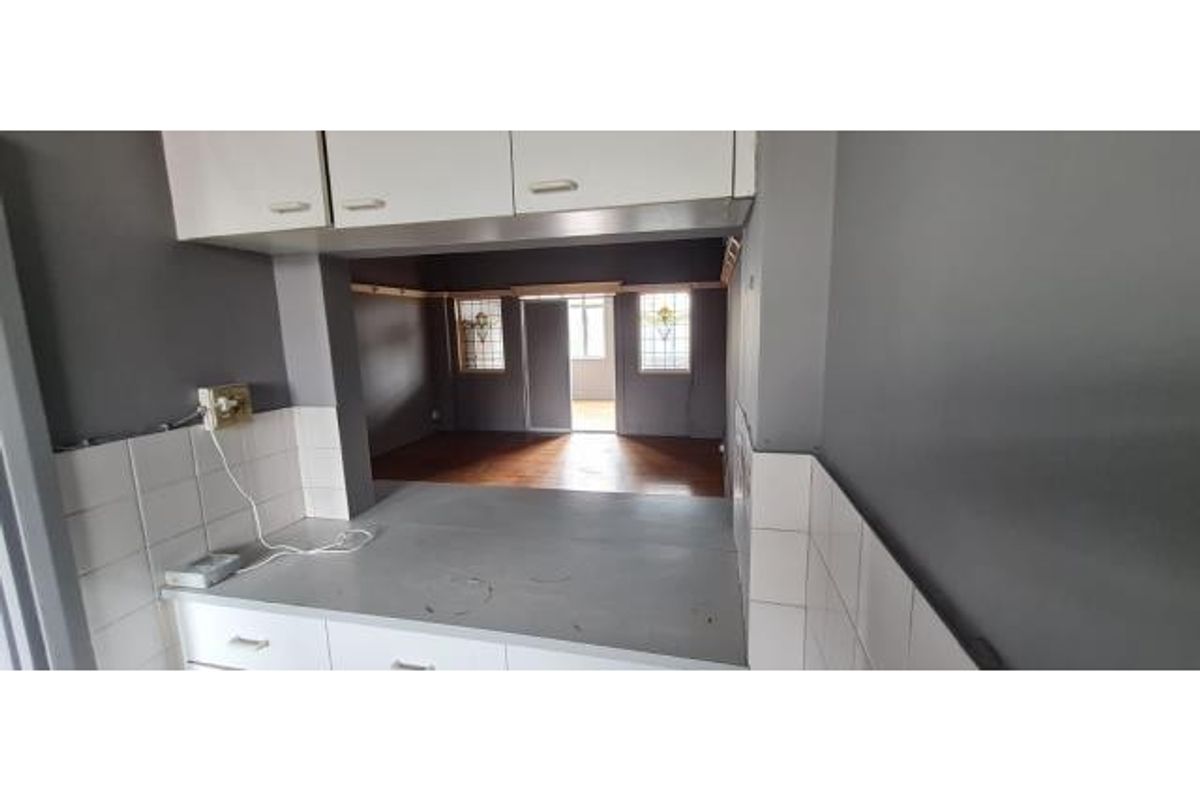 A dated kitchen featuring built-in cabinetry and a pass-through window looking into the adjacent living area, requiring cosmetic updates to the surfaces.
