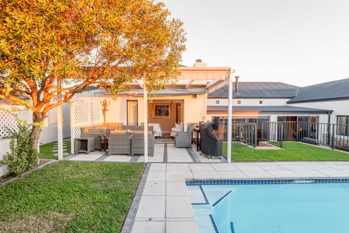 Rear exterior view featuring a paved patio area, swimming pool, and landscaped garden, providing a seamless transition to the indoor living space.