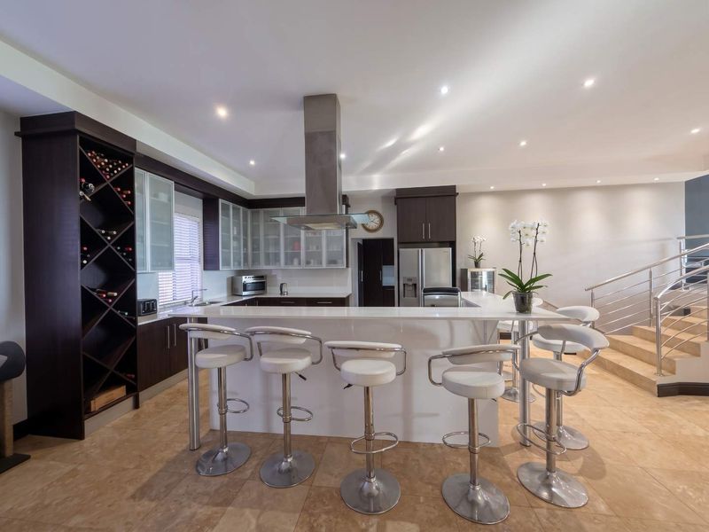 Modern kitchen featuring a large breakfast bar, stone countertops, integrated wine storage, and sleek cabinetry, seamlessly connected to the living area and staircase.