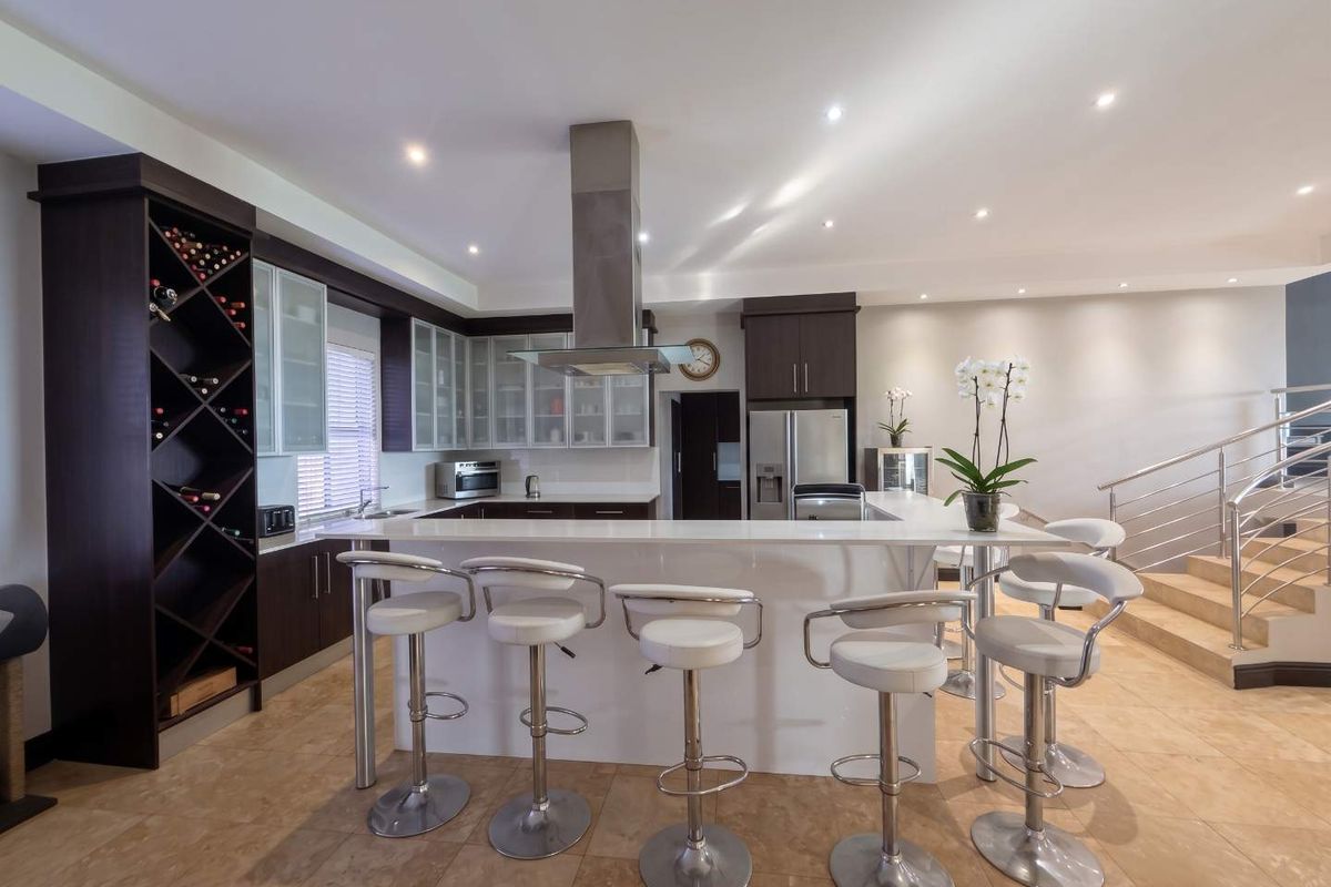 Modern kitchen featuring a large breakfast bar, stone countertops, integrated wine storage, and sleek cabinetry, seamlessly connected to the living area and staircase.
