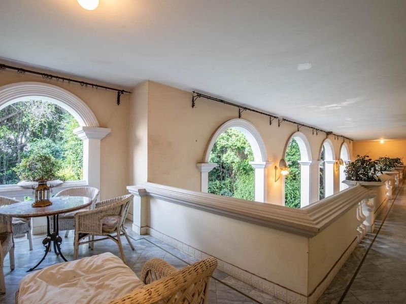 A spacious covered balcony featuring elegant arched windows, marble flooring, and classic balustrade detailing, offering a bright and airy outdoor living space.