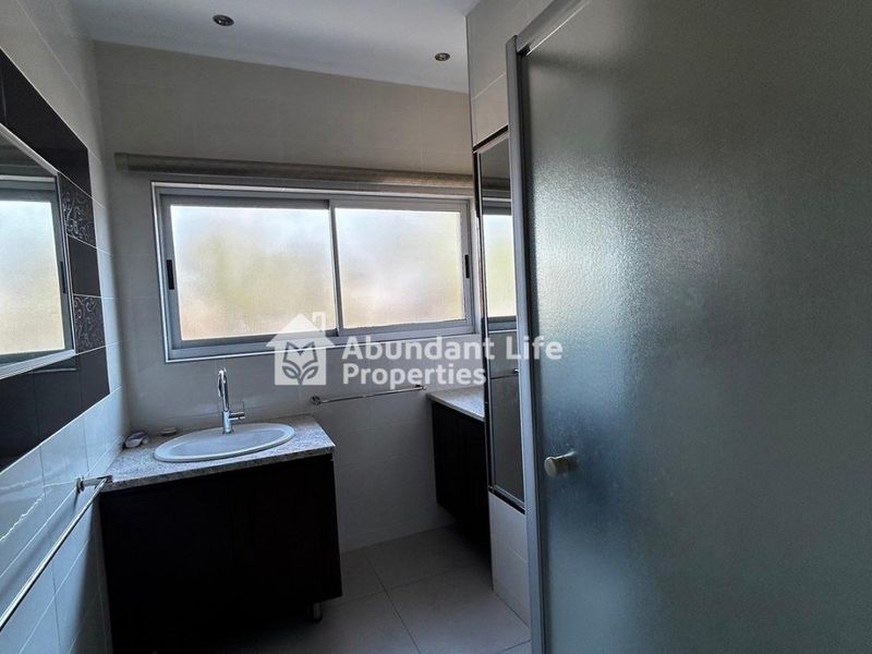 A clean, modern bathroom featuring a vanity with granite countertop, drop-in basin, and a glass-enclosed shower area with neutral floor tiling.