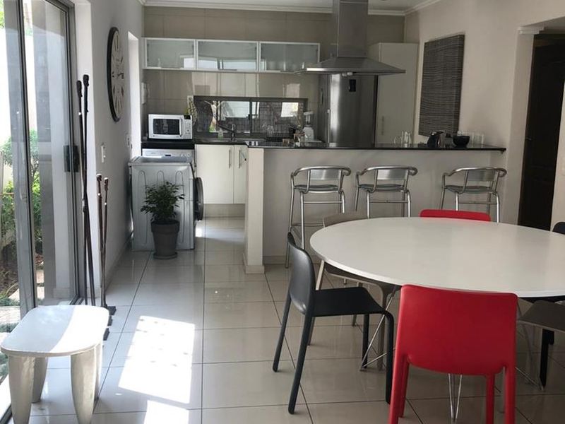 Open-plan kitchen and dining area featuring tiled flooring, modern cabinetry, a stainless steel extractor fan, and large sliding doors providing natural light.
