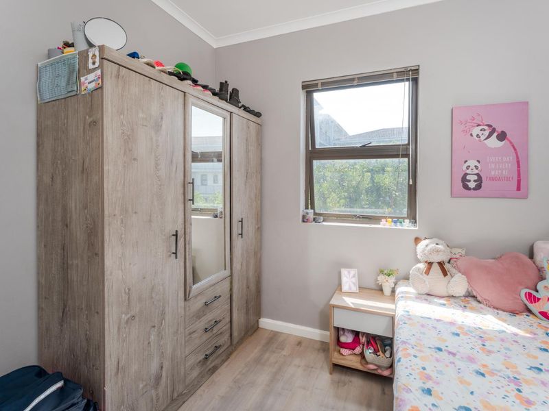 A well-maintained bedroom featuring laminate flooring, a built-in wardrobe with mirror detail, and a casement window providing natural light.