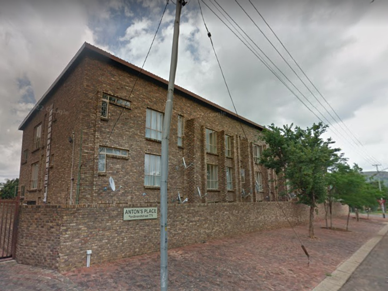 Street view of the face brick apartment building known as Anton's Place, featuring a perimeter boundary wall and paved exterior area.