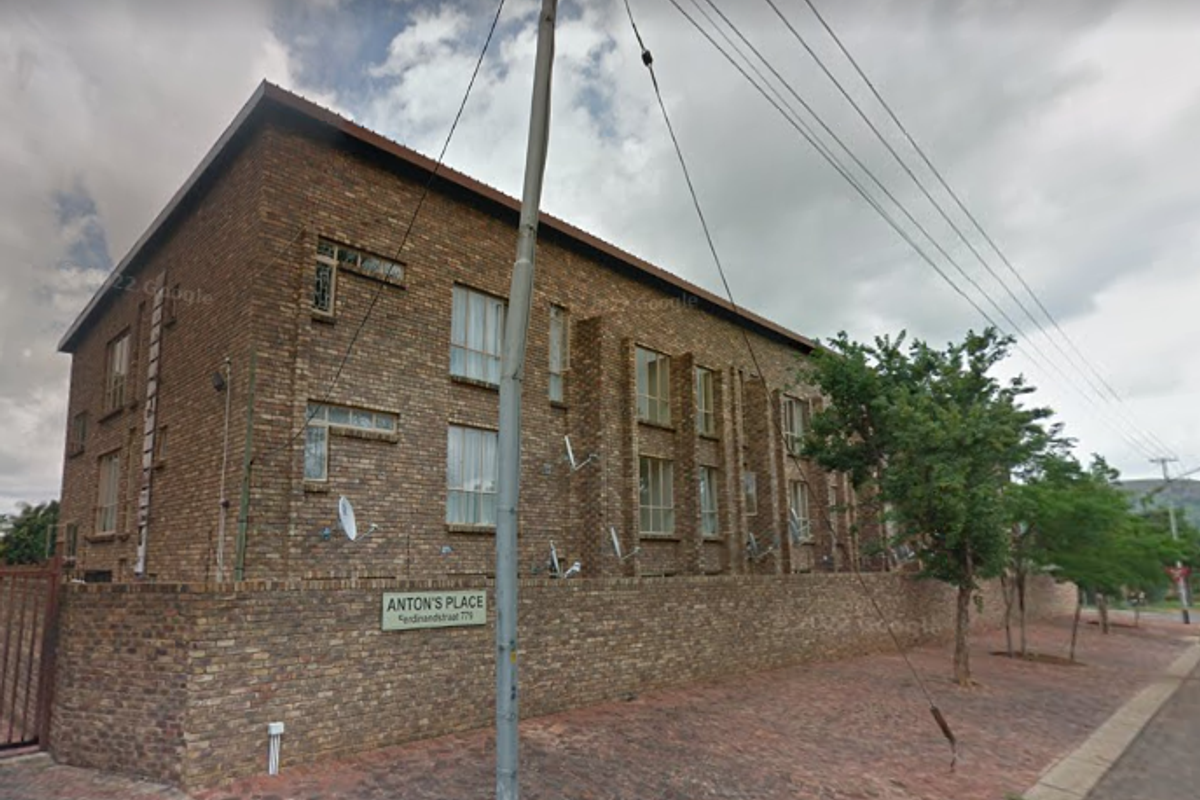 Street view of the face brick apartment building known as Anton's Place, featuring a perimeter boundary wall and paved exterior area.