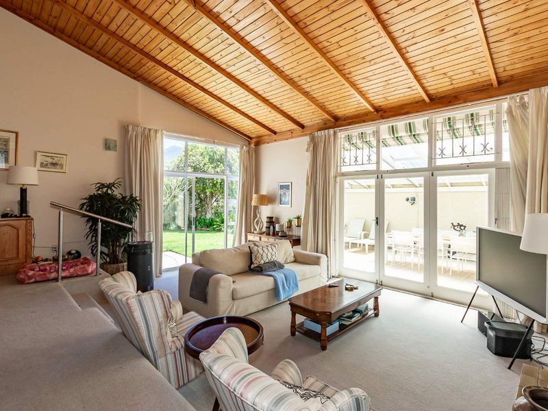 Spacious living room featuring a high vaulted timber ceiling, carpeted flooring, and large glass doors providing seamless access to the outdoor patio and garden.