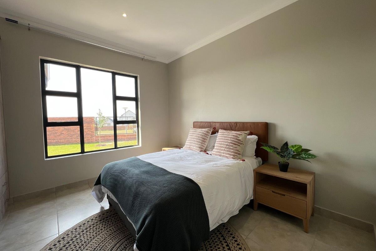 A well-lit bedroom featuring neutral wall tones, large aluminum-framed windows, and tiled flooring, offering a clean and modern living space.