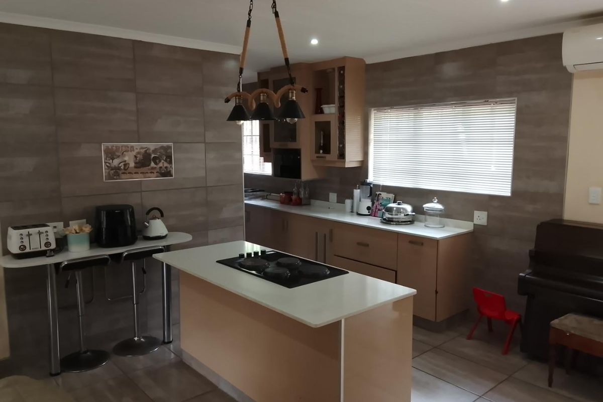 Modern kitchen featuring a central island with a built-in hob, light wood cabinetry, stone countertops, and tiled wall finishes.