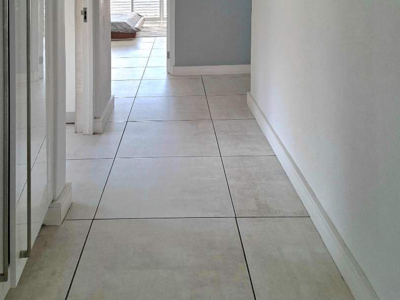 A clean, neutral hallway featuring large format floor tiles and crisp white trim, providing a bright transition between living spaces.