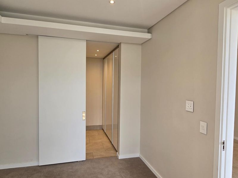A clean, modern bedroom featuring neutral tones, recessed lighting, carpeted flooring, and a sliding door leading to a walk-in closet area.