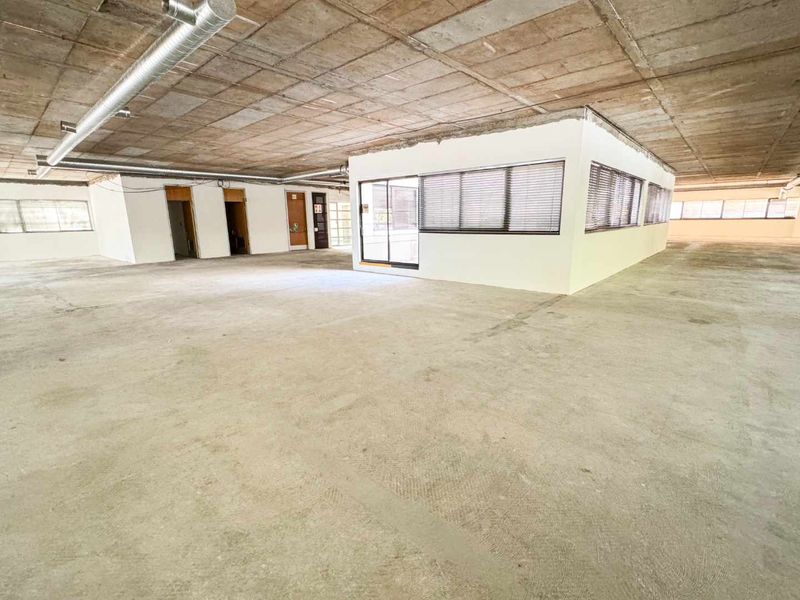 Expansive open-plan commercial space featuring an industrial aesthetic with exposed concrete ceilings, ducting, and a central partitioned office enclosure.