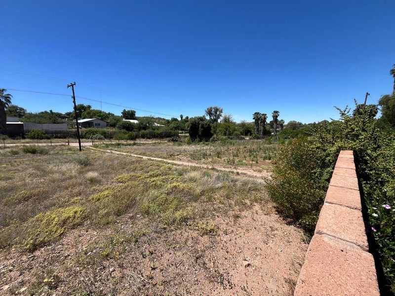 A view of the rear yard area featuring a boundary wall and open land with natural vegetation.