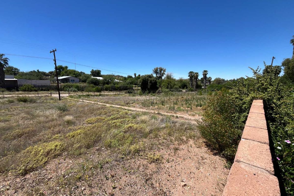 A view of the rear yard area featuring a boundary wall and open land with natural vegetation.