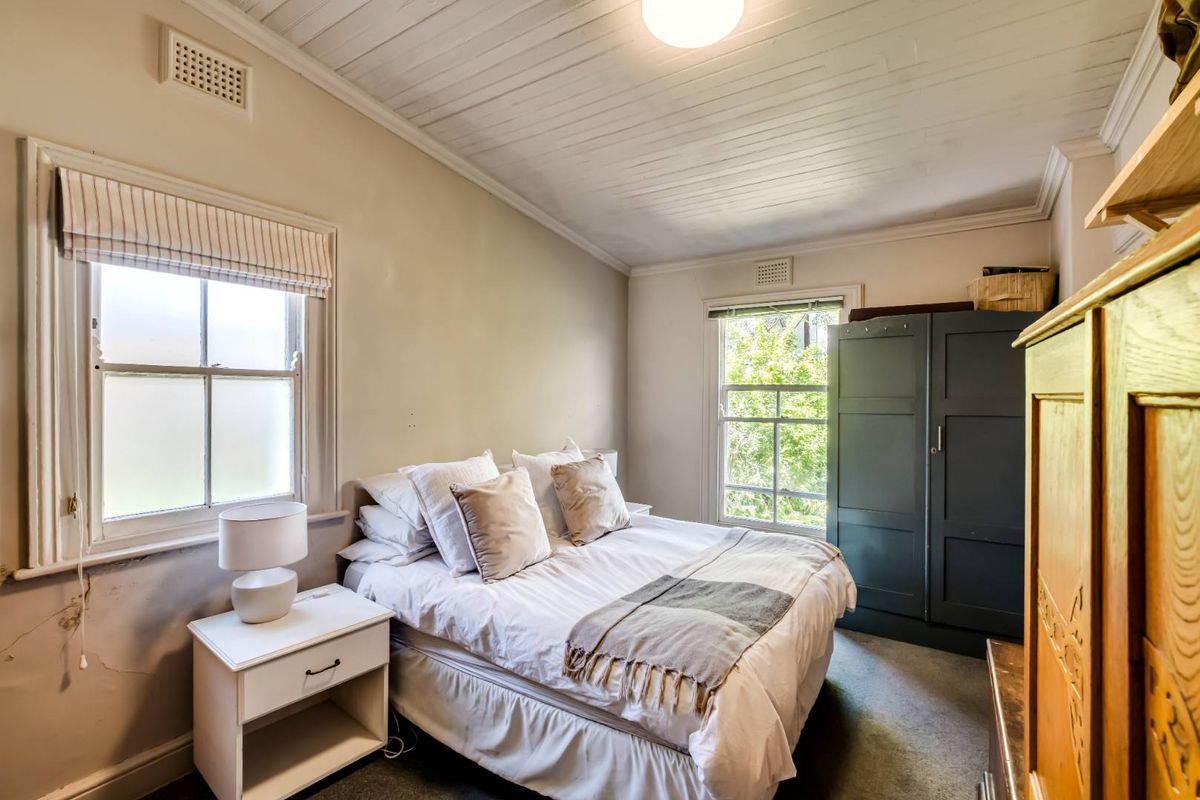 A cozy bedroom featuring timber-paneled ceilings, dual windows providing natural light, and neutral wall tones.