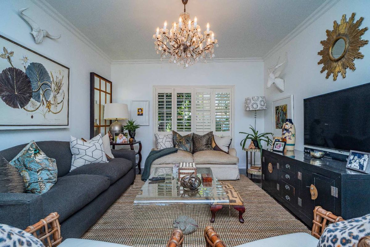A well-appointed living room featuring crown molding, plantation shutters, and a central crystal chandelier, creating a sophisticated and inviting atmosphere.