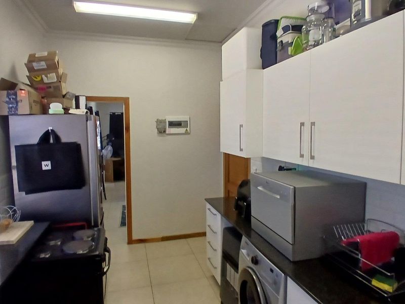 A functional scullery area featuring white built-in cabinetry, dark countertops, tiled flooring, and an integrated electrical distribution board.