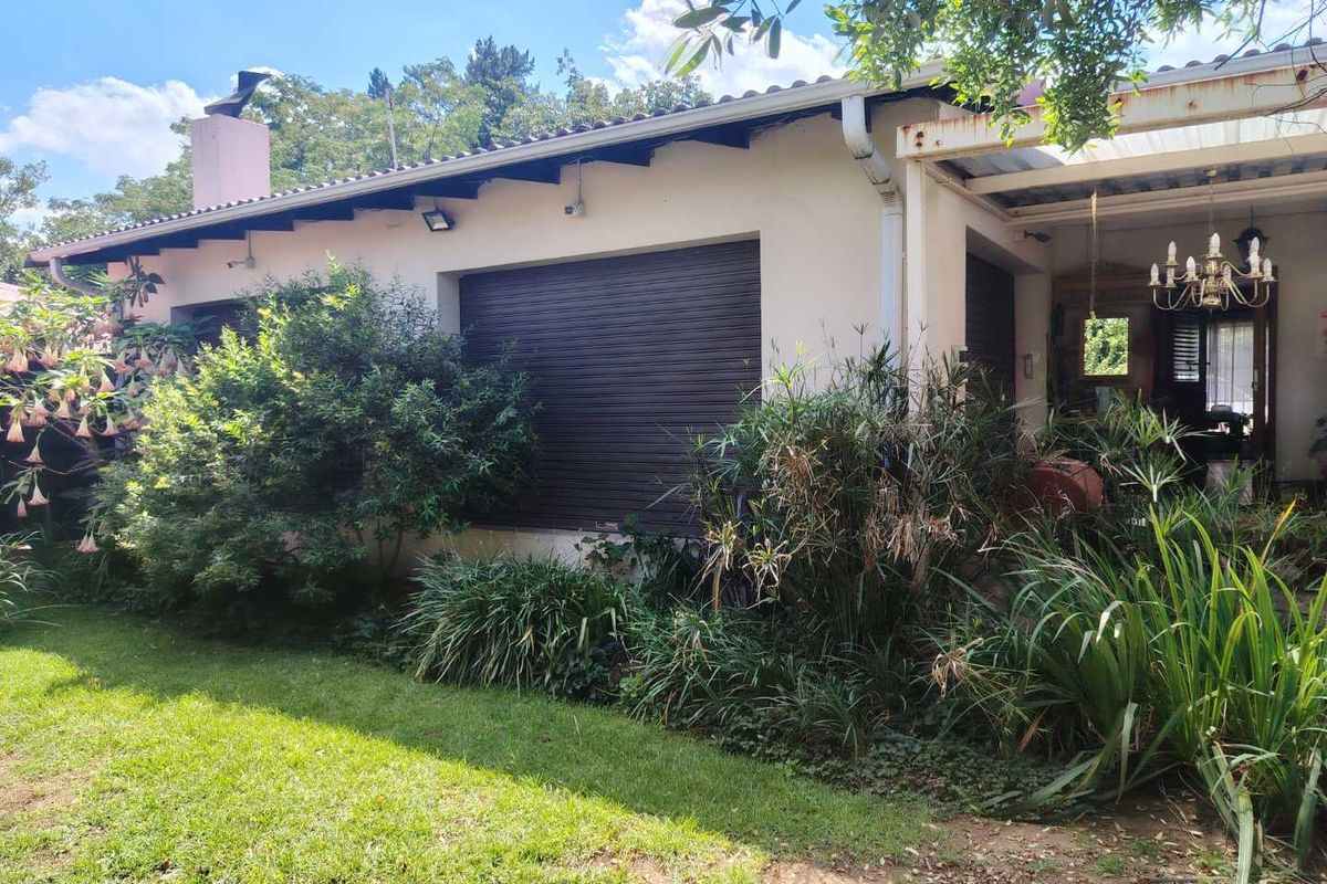 Rear view of the house featuring a covered patio area, roller shutters on windows, and a well-established garden.