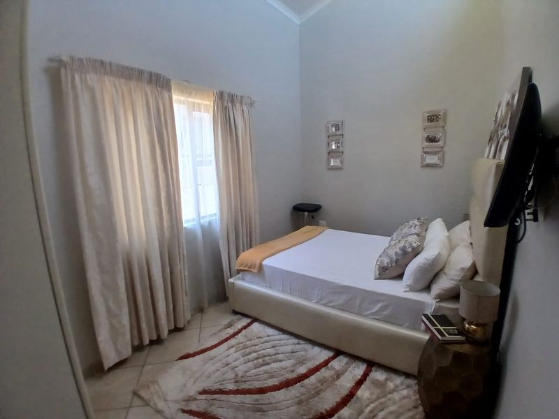 A cozy bedroom featuring tiled flooring, high ceilings, and natural light through window curtains.