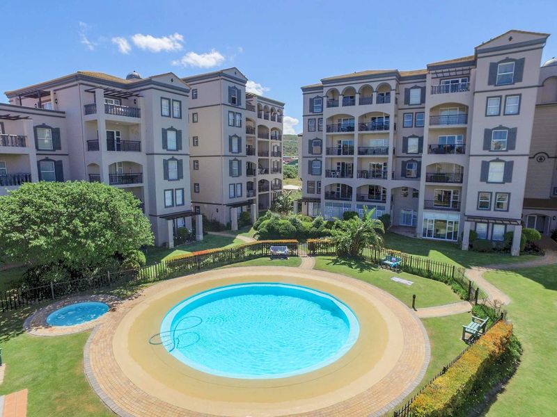 Aerial view of a well-maintained apartment complex featuring a central swimming pool, kiddies pool, landscaped gardens, and private balconies.