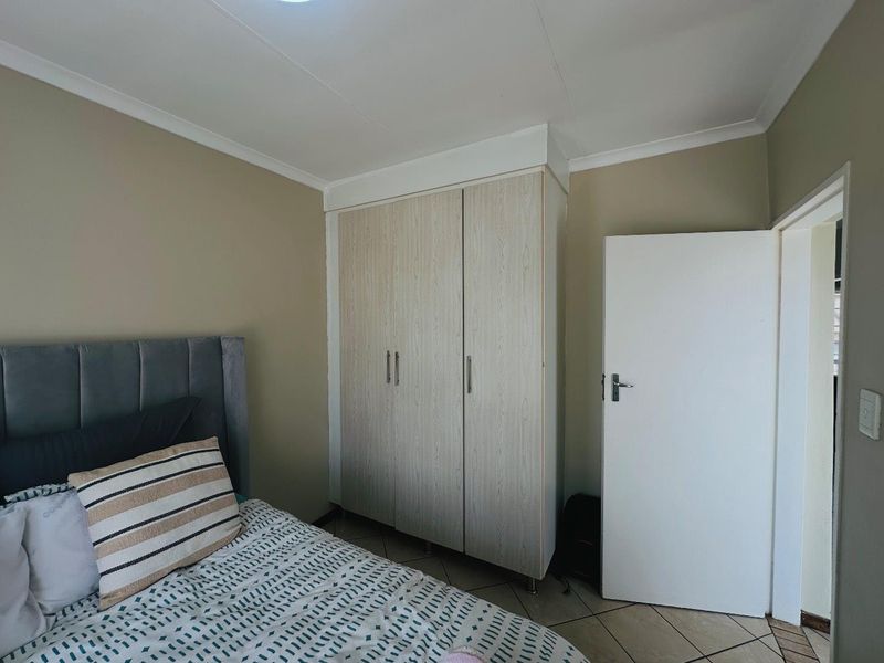 A well-maintained bedroom featuring neutral wall tones, tiled flooring, and a functional built-in wardrobe with light wood-grain finish.
