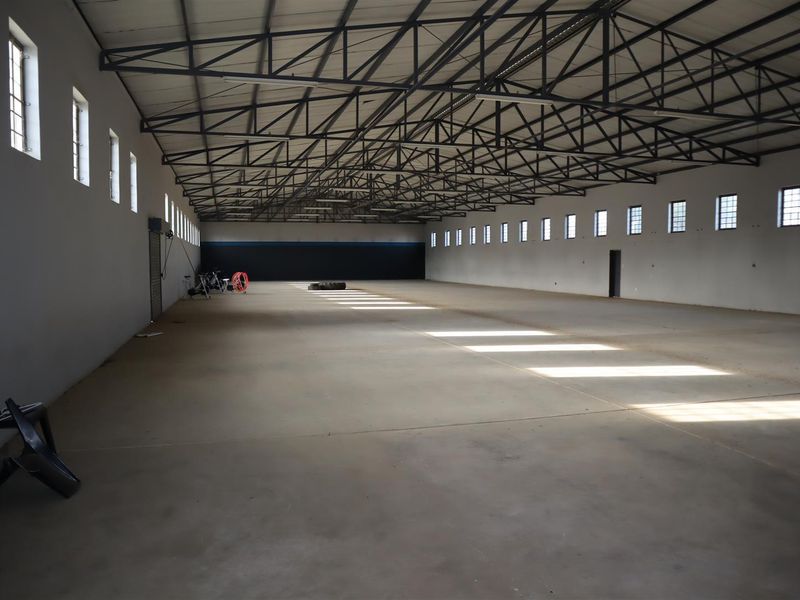 A large, open-plan utility or warehouse space featuring exposed steel roof trusses, concrete flooring, and abundant natural light from multiple high-level windows.