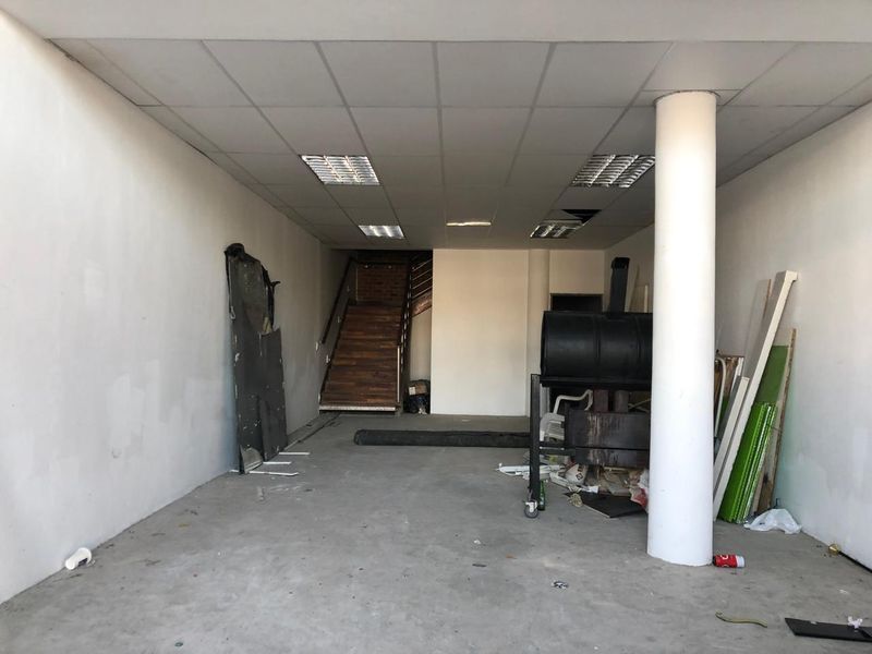 An open-plan retail space featuring a suspended ceiling, structural column, and staircase leading to an upper level, currently in need of renovation.