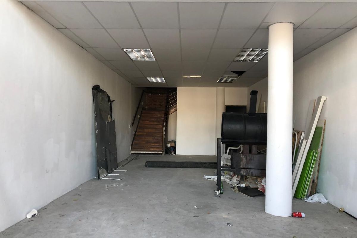 An open-plan retail space featuring a suspended ceiling, structural column, and staircase leading to an upper level, currently in need of renovation.