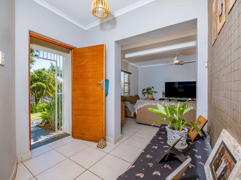 Welcoming entrance hall featuring tiled flooring, a timber front door with security gate, and a view into the adjacent living area.
