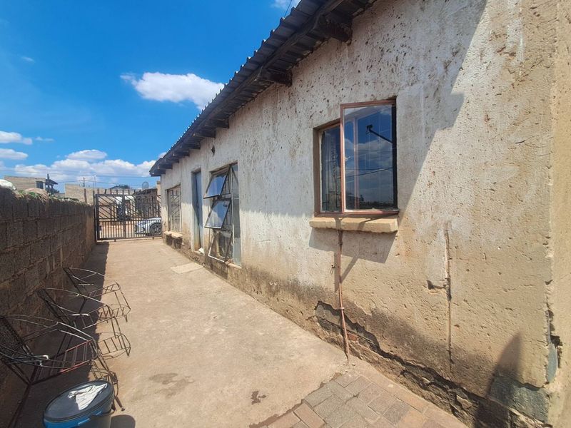 Rear exterior view of the property featuring a concrete paved walkway, boundary wall, and weathered exterior wall finishes requiring maintenance.