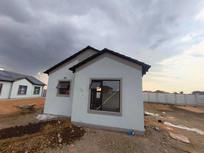 Rear view of a newly constructed house featuring a tiled roof, aluminium window frames, and an unfinished garden area with a precast boundary wall.