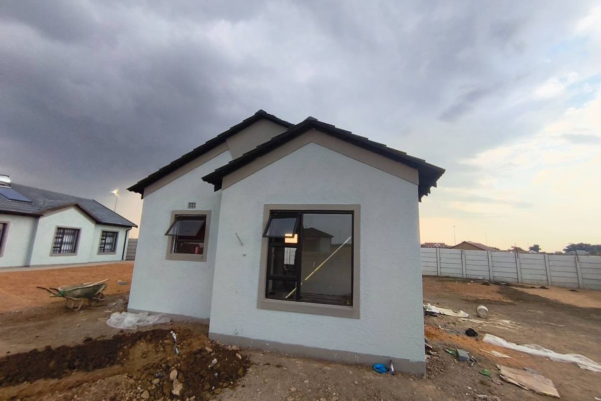 Rear view of a newly constructed house featuring a tiled roof, aluminium window frames, and an unfinished garden area with a precast boundary wall.