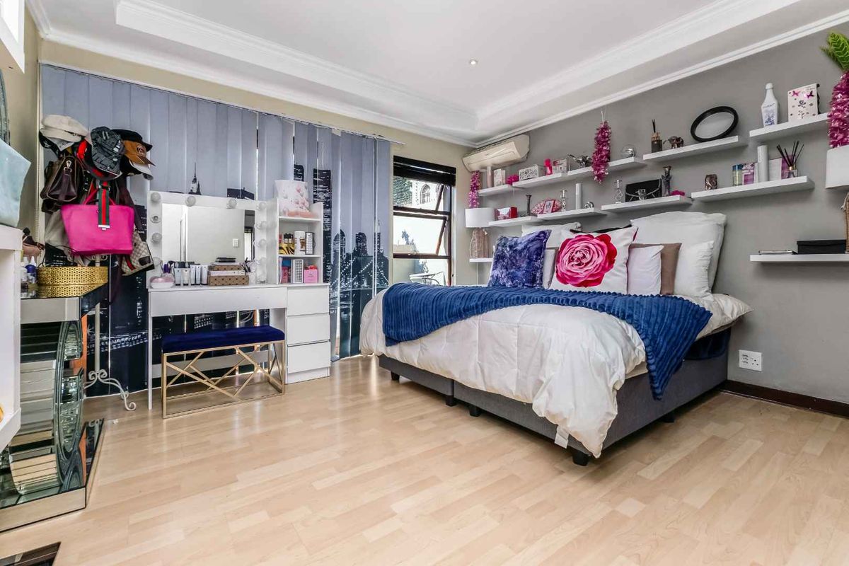 A well-maintained bedroom featuring light wood-look flooring, crown molding, wall-mounted shelving, and a split-system air conditioning unit.